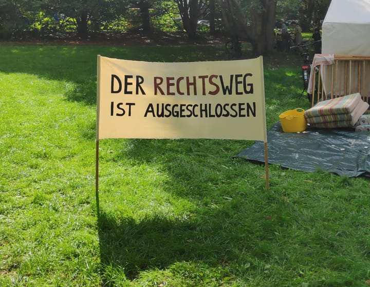 Ein Textiltransparent, aufgestellt auf einer grünen Wiese, mit der Aufschrift "Der Rechtsweg ist ausgeschlossen".